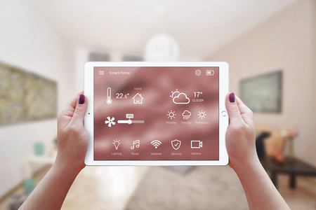 Smart remote home control app in woman hand. Living room interior in background.の写真素材