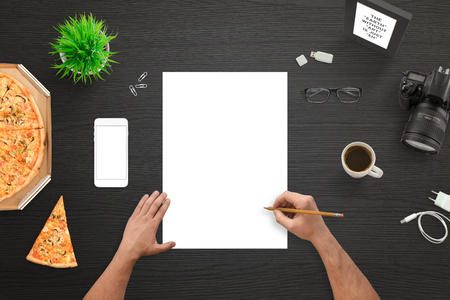 Designer or photographer sketching on empty white paper. Camera and mobile phone beside. Top view of black work desk.の写真素材
