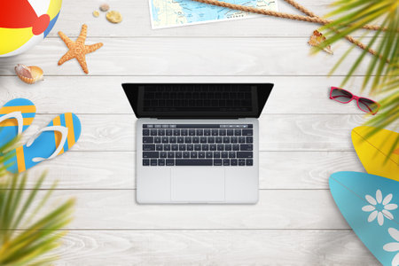 Laptop na white wooden desk surrounded by objects for summer vacation. Top view. Blank screen for...