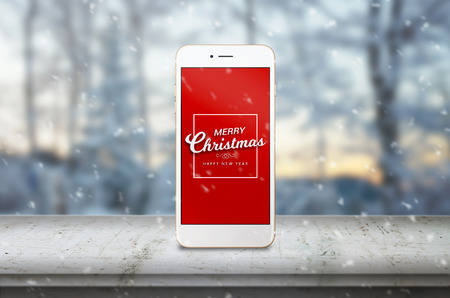 Mobile phone on desk with Merry Christmas massage. Snow and winter landscape in background.の写真素材