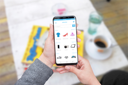 Online store web site or app on modern smart phone screen with round edges. Coffee shop in background.の写真素材
