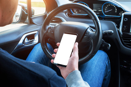 Driver use smart phone in car. Isolated screen for mockup. Modern car interior in background.の写真素材