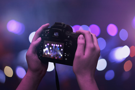 Camera in hands. Bokeh and concert, live music lights in background.の写真素材