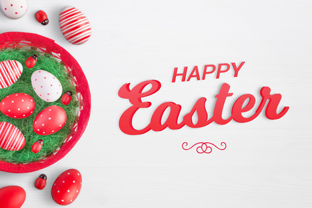 Happy easter text on white surface with eggs, basket and ladybug decorations beside.の写真素材