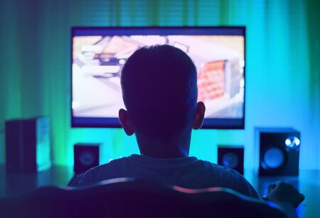 Boy as anonymous, using a computer or playing a game. View from back.の写真素材