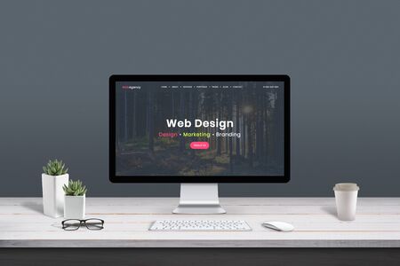 Web design studio concept. Work desk with computer display and modern design web agency page.の写真素材