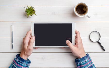 Tablet in hand mockup on work desk. Top view, flat lay composition. Close-up. White wooden desk.の写真素材