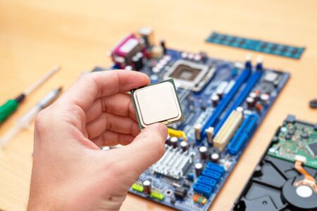 Computer processor in hand. Motherboard is ready for installation in background. Beside is hard drive, memory and screwdriver.の写真素材