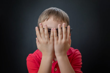 The boy peeks through his fingers. Watching a  scary movie with 3d glasses.