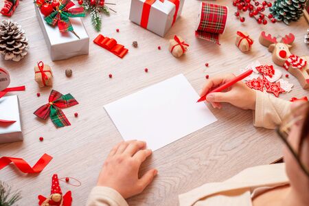 Girl writes on paper surrounded by lots of Christmas gifts and decorations. Paper is blank, to add greeting card text.の写真素材