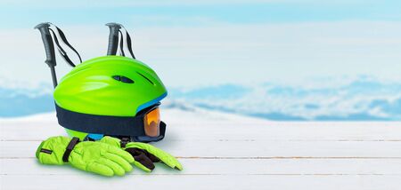 Ski equipment on a white wooden table. Helmet, gloves, glasses nad poles. Copy space beside. Snowy mountain peaks in the backgroundの写真素材
