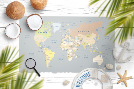 World map on a white wooden table surrounded with coconut, palm leaves, shells, starfish, lifebelt,...