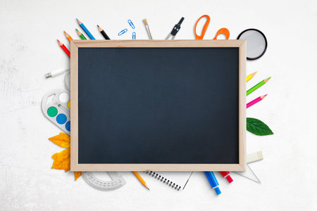 Empty chalkboard for promo text surrounded by school supplies on white desk. Top view, flat lay,...