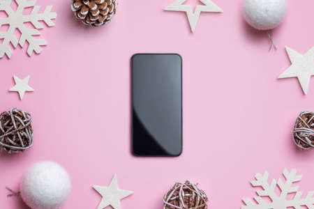 Phone on pink desk surrounded by Christmas decorations. Concept of Christmas shopping and gift wrapping. Blank smart phone for mockupの写真素材