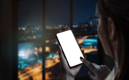 Woman use smart phone by the window. City lights in background. Isolated display for mockup, app design promotionの写真素材