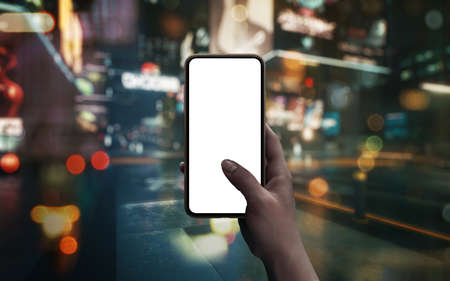 Phone with blank screen in woman hand on city street at night. Bokeh in backgroundの写真素材