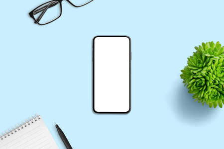Phone mockup on blue office desk. Minimal composition with plant, pad, pen and glassesの写真素材