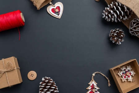 Christmas composition on black surface with red details on Christmas decorations. Christmas gift, pine cones, wooden decorations, red thread, tailoring button. Flat lay, top view, copy spaceの写真素材