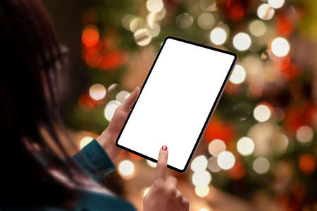 Tablet mockup in woman hads with a lot of Christmas bokeh lights in background. Isolated display for content promotionの写真素材
