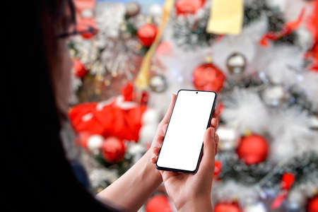 Girl with a phone front of a Christmas tree. Isolated phone display for app or greeting text promotionの写真素材