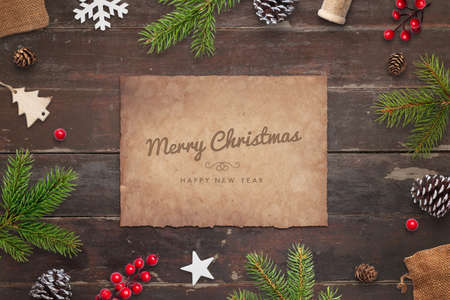 Merry Christmas and Happy New Year greeting card on old paper, surrounded by Christmas decorations on wooden tableの写真素材