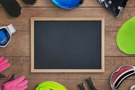 Clean chalkboard surrounded by ski equipemnt on wooden table. Copy space for text promotion. Top view, flat lay compositionの写真素材