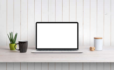 Lapop on desk with isolated white screen for mockup, app or web page design promotion. White wooden wall in backgroundの写真素材
