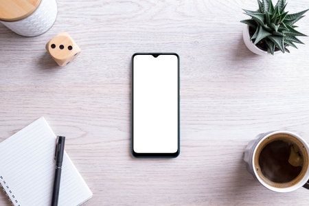 Flat lay phone mockup composition on work desk. Isolated screen for app presentation. Pad with pen, coffee mug, plant and box beside. Clean office deskの写真素材