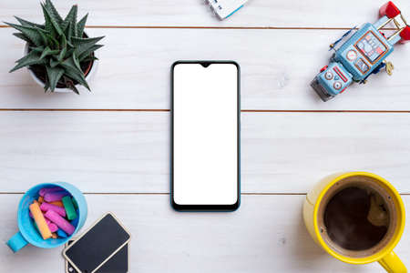 Creative work table flat lay composition with smart phone mockup surrounded by robot toy, coffee mug, plant and colored chalkの写真素材