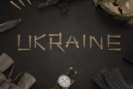 Ukraine war concept. Ukraine text written with bullets from an automatic rifle and surrounded by military equipmentの写真素材