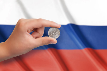 Russian ruble coin in hand. Fag of Russia in the backgroundの写真素材