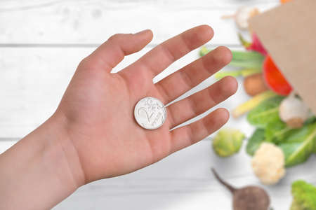 Russian ruble coin in hand. The concept of inflation and consumer basket buying. In the background is a bag of food and groceriesの写真素材
