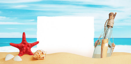 White paper stuck in the sand of the beach, surrounded by starfish, shells and a bottle with a message. Clean surface for promo textの写真素材