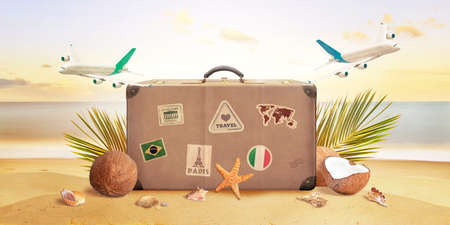 Retro suitcase on tropical beach surrounded by planes, palm leaves, coconuts and shells. Summer travel concept compositionの写真素材
