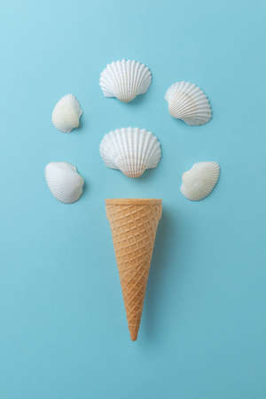 Shellfish ice cream concept on blue surface. Ice cream cone with white shells.の写真素材