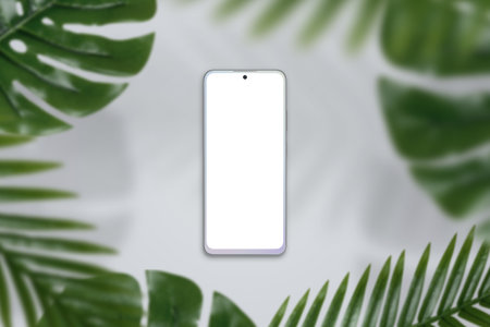 Phone mockup on gray surface surrounded by green leafs. Top view, flat lay compositionの写真素材