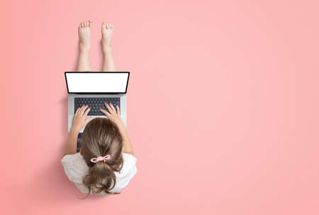 Little girl works on a laptop computer. View from above. Isolated screen for mockup, website or game promotion. Copy space beside on red backgroundの写真素材