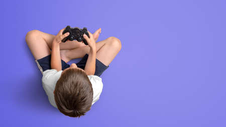 Boy holding gamepad and play game. Top view. Copy space on purple surface. Gaming conceptの写真素材
