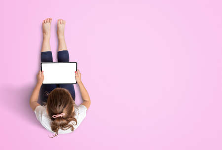 Child sitting and working on the tablet. White screen for app or game promotion mockup. Free space for copy on pink background. View from aboveの写真素材