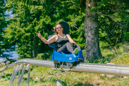 Woman with sunglasses rides a mountain roller coaster with a thumbs up. Warm summer day on the...