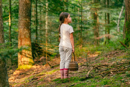 Girl with a basket lost. Stands in the forest alone and looks at the treesの写真素材