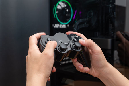 Gamepad in hand with modern gaming PC case in background. PC gaming conceptの写真素材