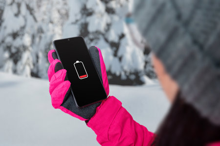 Woman holding smart phone with charging battery on the screen in winter.の写真素材
