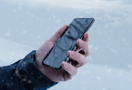 Closeup of a man's hand holding a smartphone in the snowの写真素材