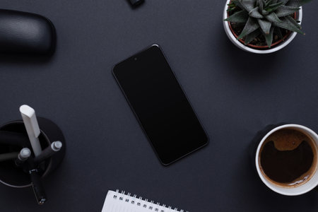 Minimalist and organized work desk with a blank smart phone surrounded by a plant, pens, coffee and notepad. Blank screen for mockup app presentation. Office work desk composition, top view, flat layの写真素材
