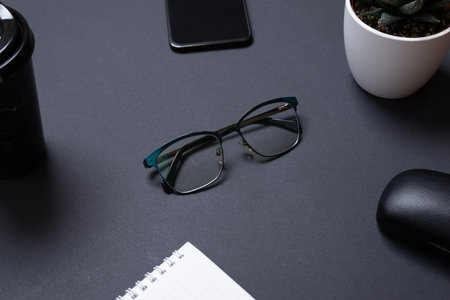 Glasses on black office desk surrounded by office supplies. Modern business compositionの写真素材