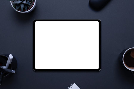 Tablet mockup on black desk with plant, pens, coffee mug, glasses box, and pad,. Top view, flat lay compositionの写真素材