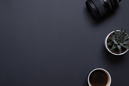 Photographer work desk composition with camera lens, plant and coffe mug. Top view, flat lay with copy space on black deskの写真素材