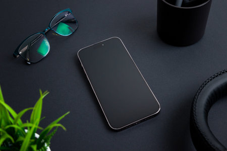 Phone placed on black desk among office items like a headset, plant, glasses, and a coffee mug