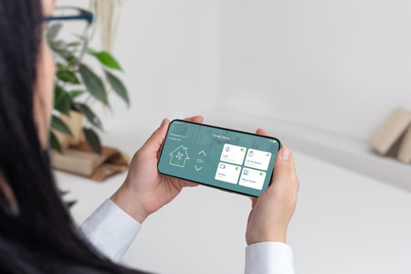 Integration of technology and home comfort concept. Woman holding a mobile phone, controlling a...